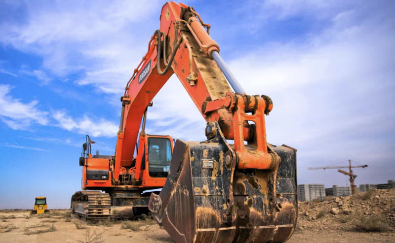 Orange excavator with hydraulic boom cylinders on a jobsite.