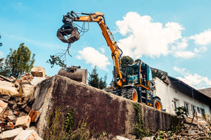 a backhoe lifting a tree branch in front of a home renovation project
